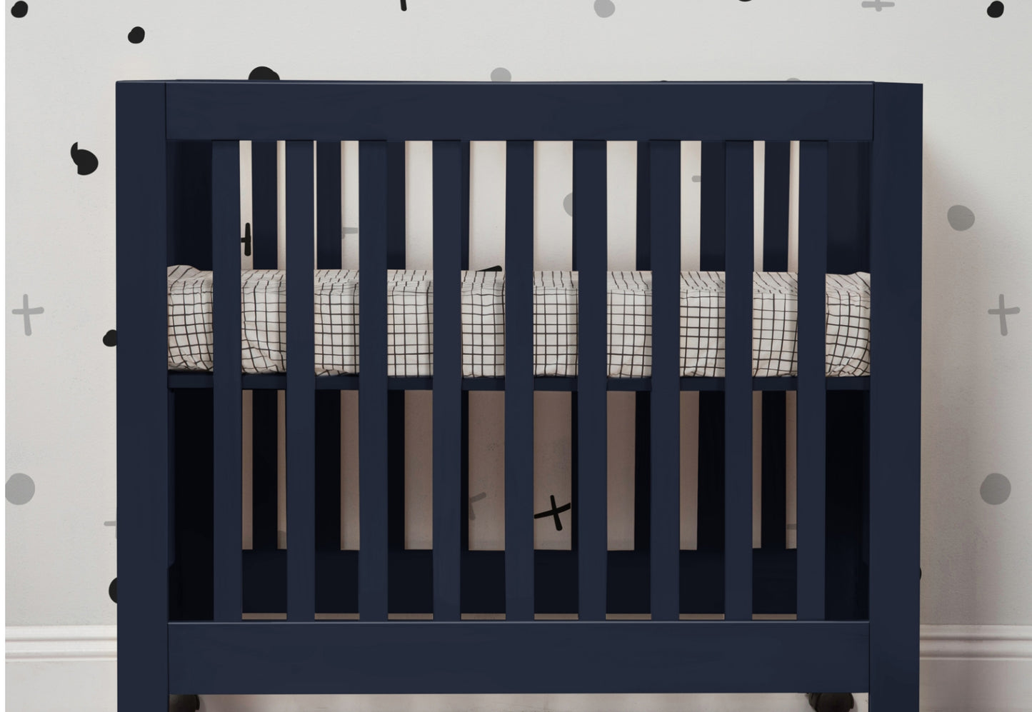 A navy blue crib with a grid-patterned bedding set against a wall adorned with black and plus sign decals.