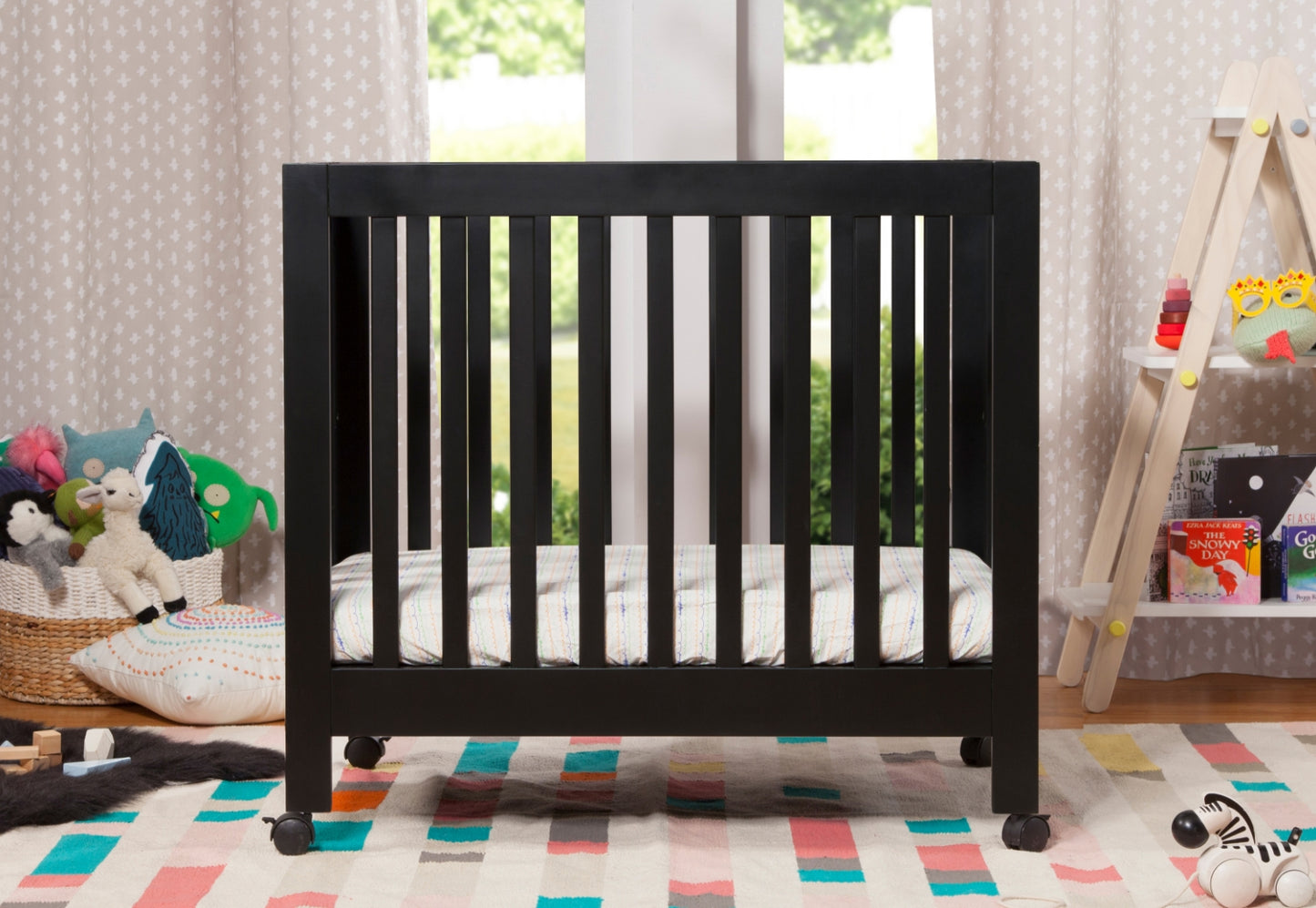 A black baby crib with a white mattress in a nursery room, surrounded by toys and decorated with colorful accents.