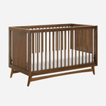 Classic wooden crib with slatted sides and a white mattress, isolated on a plain background.