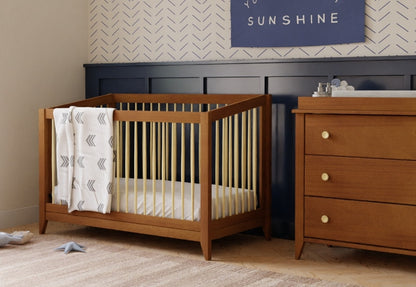 A stylish nursery featuring a wooden crib and matching dresser set against a herringbone wall with a decorative sign saying "SUNSHINE" above.