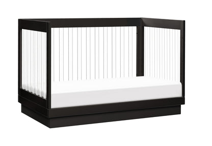 Modern black crib with a white mattress and transparent safety rails, isolated on a white background.