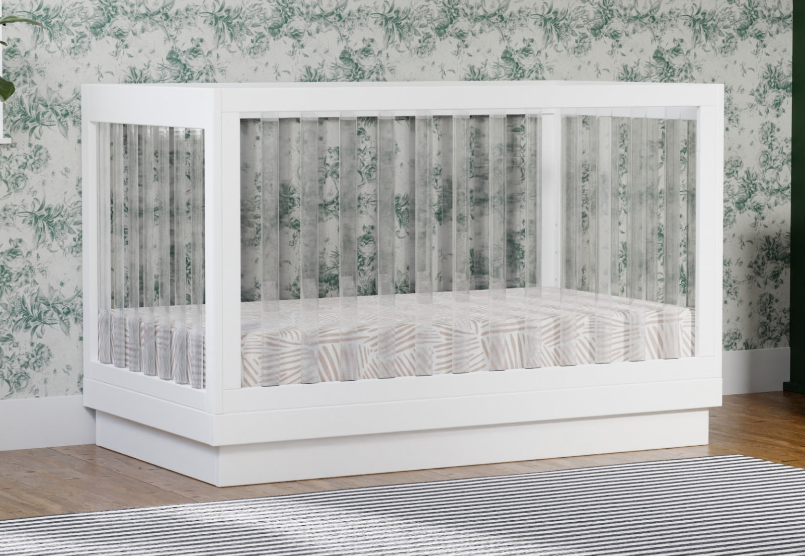 A modern white baby crib in a nursery with floral wallpaper.