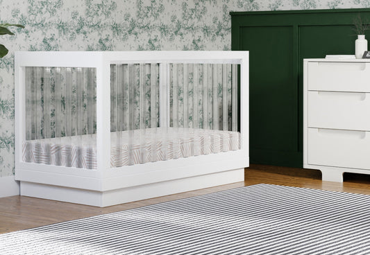 Modern white crib in a stylish nursery with floral wallpaper and dark green accents.