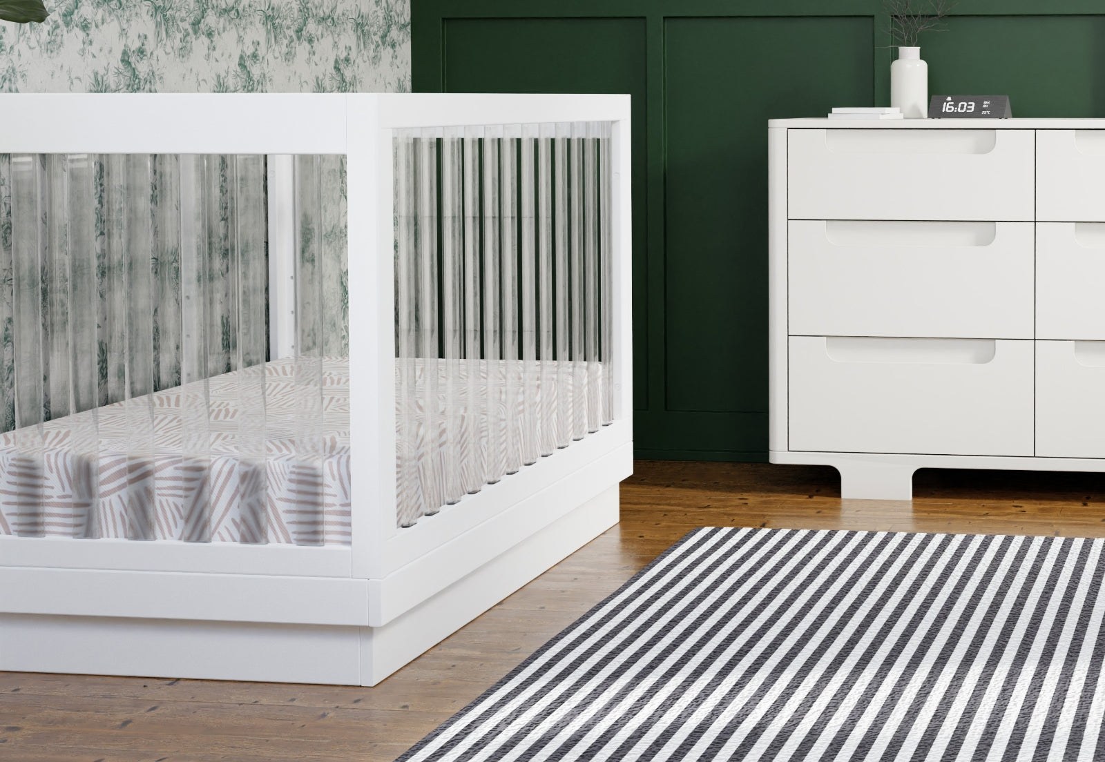 Modern nursery featuring a stylish white baby crib beside a sleek white dresser, complemented by a green wall and a striped rug.