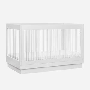 A modern white baby crib with vertical slats and a solid base.