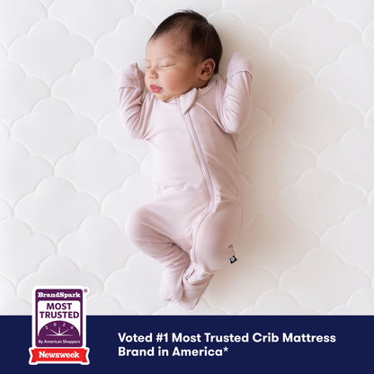 A baby in a light pink onesie sleeps on a Newton Baby Crib Mattress, which is breathable and washable. A corner badge states "Most Trusted Crib Mattress Brand in America," citing Newsweek and BrandSpark as sources.