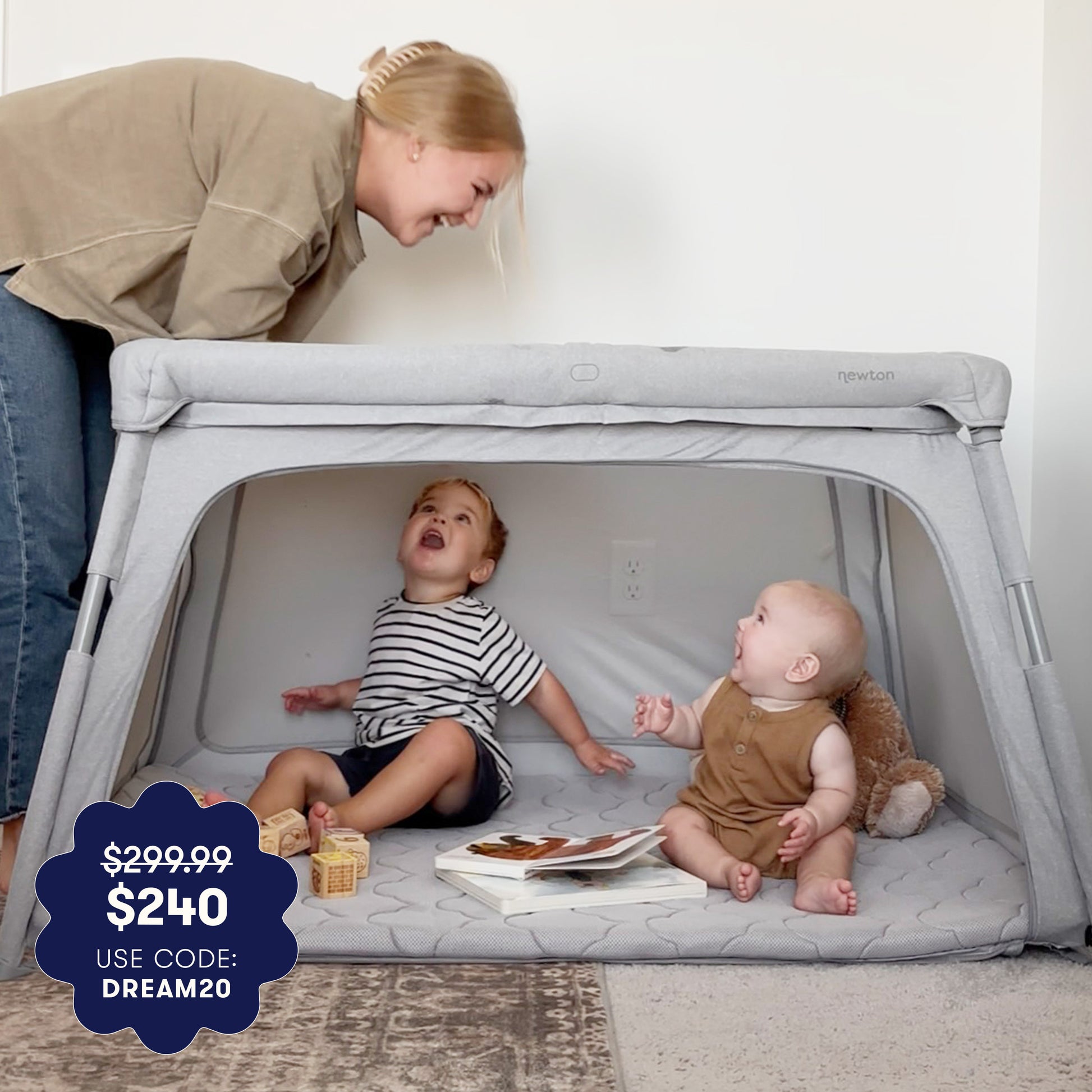 Two children playing inside a portable playpen with a woman looking in, on a light background. 999-5100-GRY