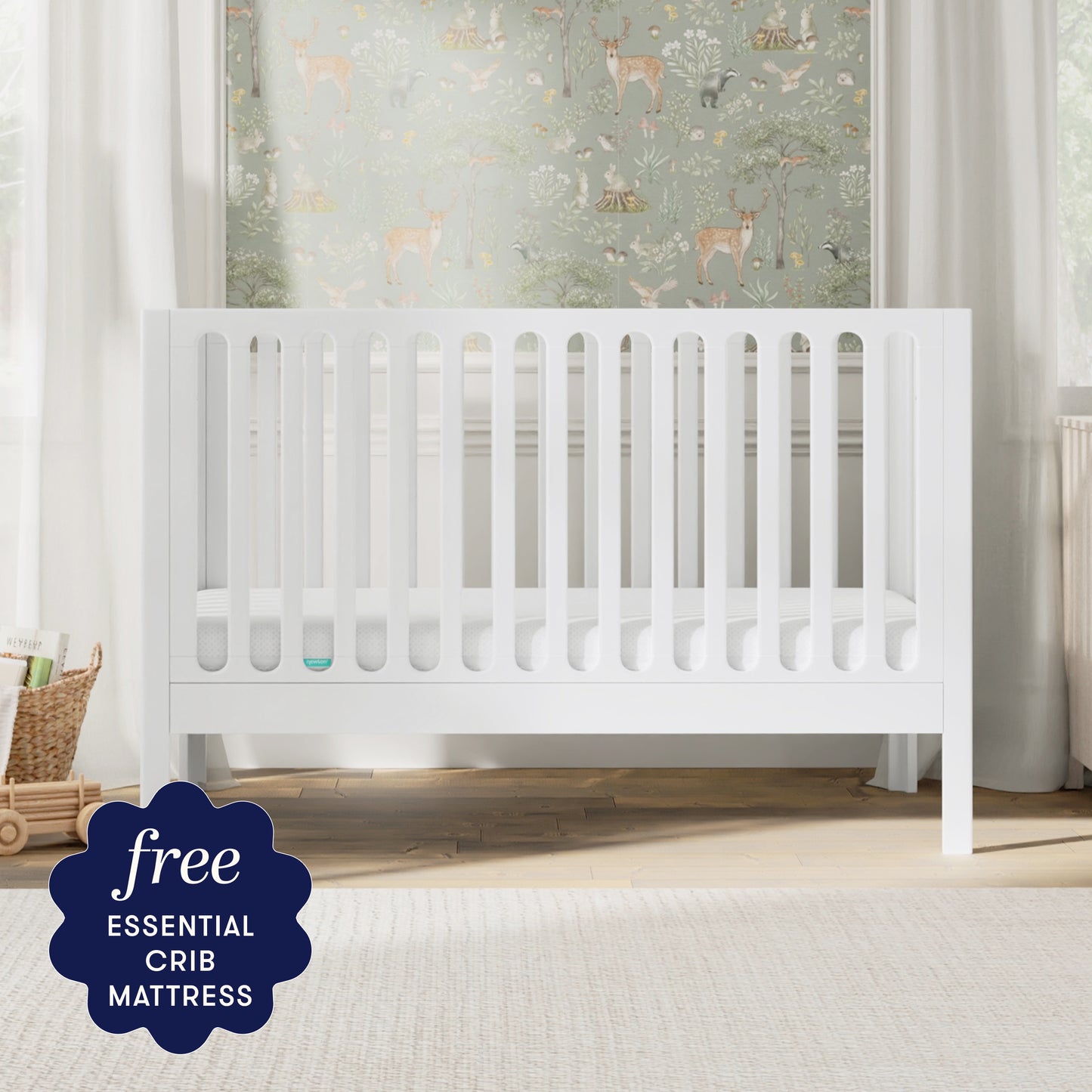 A white Newton Galileo Convertible Crib by Newton Baby, complete with a mattress, stands in a bright nursery decorated with nature-themed wallpaper. A badge in the corner reads: “Free ESSENTIAL CRIB MATTRESS.”.