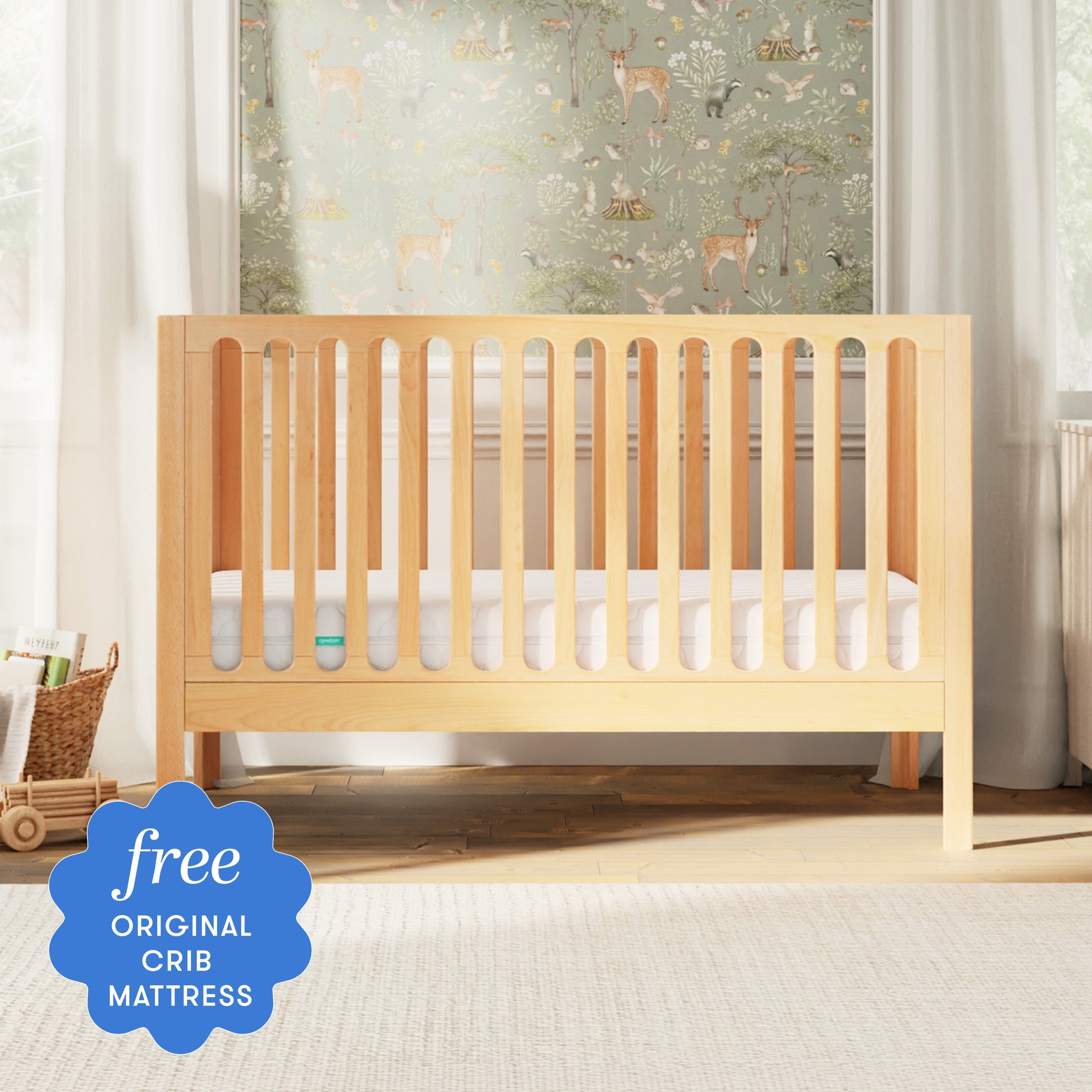 The Newton Baby Newton Galileo Convertible Crib, featuring a white mattress, stands in a bright nursery with animal-themed wallpaper. A blue badge in the corner reads, “free original crib mattress.”.