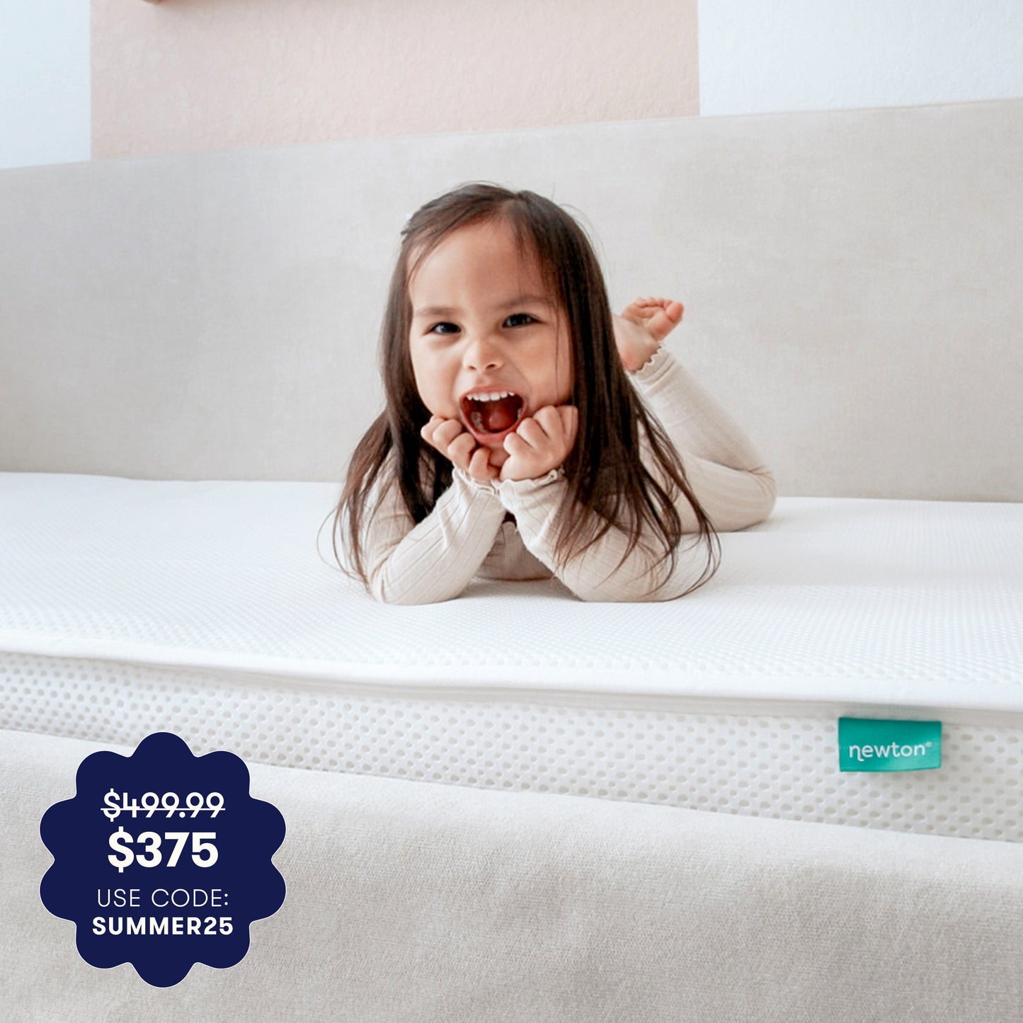 A young child with long dark hair and a big smile lies on a GREENGUARD Gold certified, breathable Newton Baby Kids' Twin Mattress. A badge reads “$499.99 $375 Use code: SUMMER25.” The tag on the washable kids mattress says “newton.”.