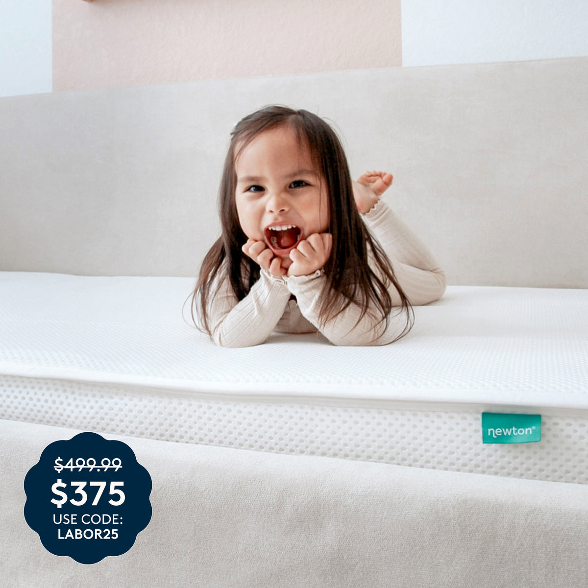 A young child smiles and lounges on the Kids’ Twin Mattress by Newton Baby, which features a white, washable cover and a beige headboard. A sale badge in the corner displays $375, was $499.99, use code: LABOR25. The breathable mattress is GREENGUARD Gold certified for your peace of mind and includes the signature green Newton tag.