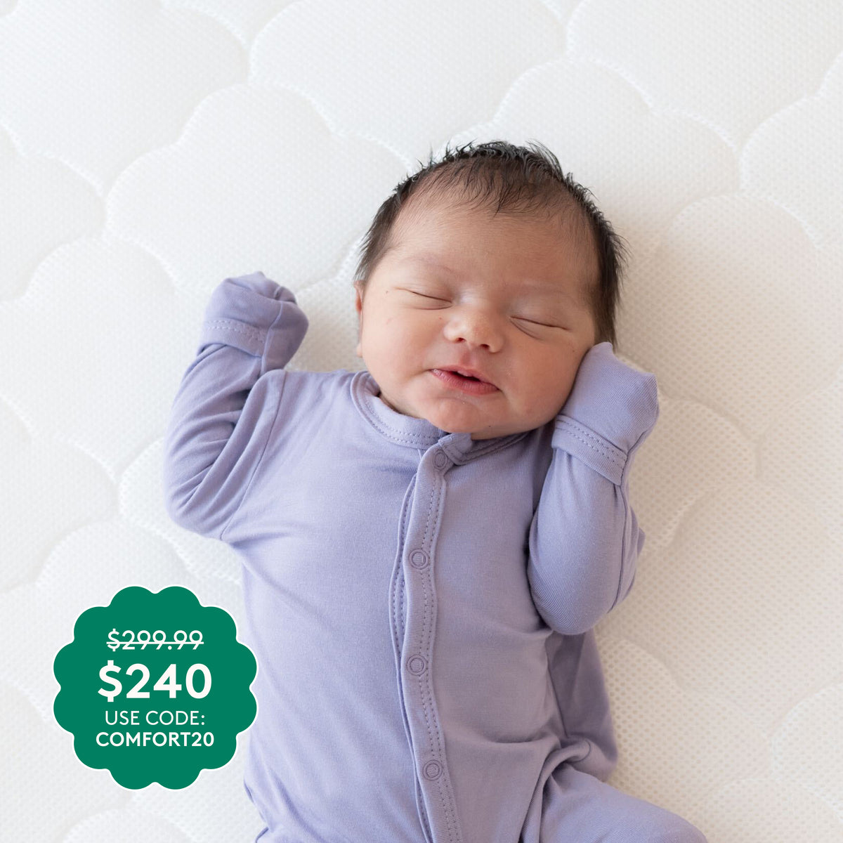 A newborn in a lavender onesie smiles while resting on the Newton Baby Crib Mattress. Price tag: $299.99 $240 USE CODE: COMFORT20.