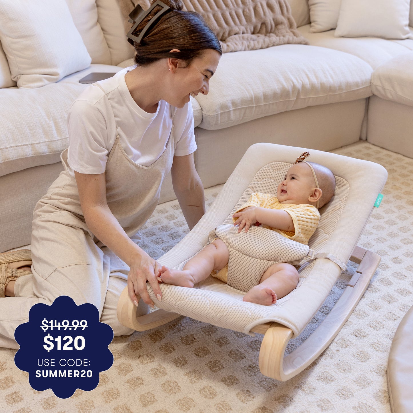 A smiling woman kneels beside a baby in the Newton Baby Rocker by Newton Baby, relaxing in a cozy living room. A promo badge shows $149.99 $120 USE CODE: SUMMER20.