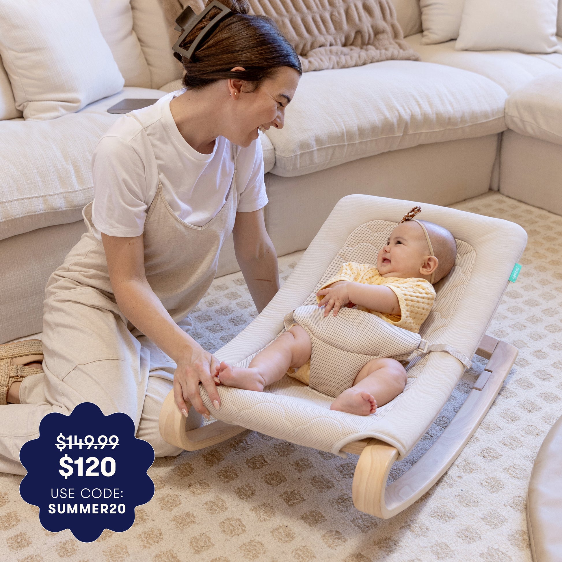 A smiling woman kneels beside a baby in the Newton Baby Rocker by Newton Baby, relaxing in a cozy living room. A promo badge shows $149.99 $120 USE CODE: SUMMER20.