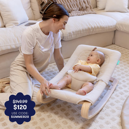 A smiling woman kneels beside a baby in the Newton Baby Rocker by Newton Baby, relaxing in a cozy living room. A promo badge shows $149.99 $120 USE CODE: SUMMER20.