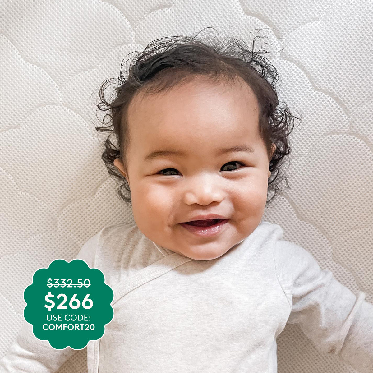 A smiling baby in a light onesie lies on a textured white surface atop the ultra-breathable Newton Baby Waterproof Crib Mattress. A green label shows $266 (was $332.50) with promo code COMFORT20.