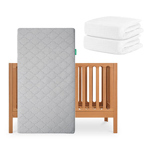 The Newton Baby Galileo Crib with the Original Crib Mattress (gray, breathable) leaning against it, plus two neatly folded organic cotton sheets beside. skip