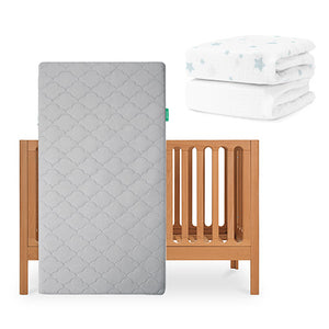 The Newton Baby Galileo Crib is shown with the Original Crib Mattress in gray, and a stack of two folded organic cotton sheets with blue star patterns in the background. skip