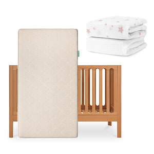 The Newton Baby Galileo Crib stands upright with the Original Crib Mattress; nearby are a folded white crib sheet with pink stars and a plain organic cotton sheet from the Galileo collection. skip