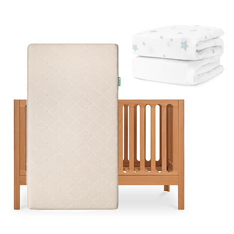 The Galileo Crib by Newton Baby features the Original Crib Mattress standing in front. Nearby are two folded crib sheets from Newton Baby, one of which displays a blue star pattern. skip