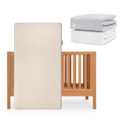 The Newton Baby Galileo Crib stands upright with the Original Crib Mattress in beige. To the right, two folded fitted sheets—one gray with white stars and one solid white—complete this cozy Newton Baby setup. skip