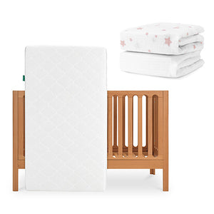 The Newton Baby Galileo Crib with the Original Crib Mattress stands upright. In the top right, folded Newton Baby sheets—one organic cotton with pink stars and one plain white—are stacked neatly. skip