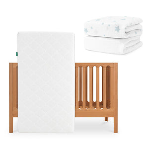 The Newton Baby Galileo Crib is shown with the Original Crib Mattress propped against it. In the upper right, two folded white Newton Baby sheets are visible—one featuring a blue star pattern. skip