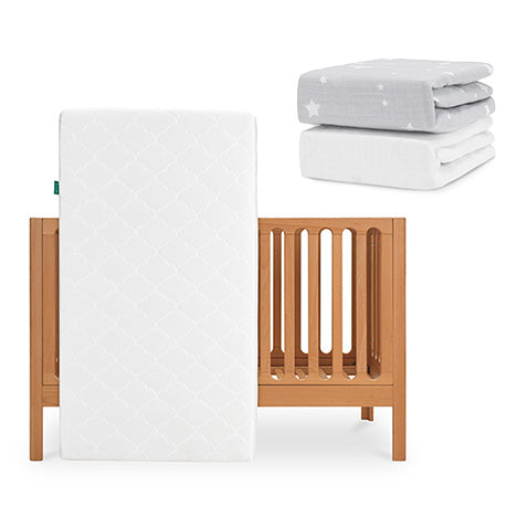 The Newton Baby Galileo Crib stands upright with the Original Crib Mattress inside. Above and to the right, two Newton Baby sheets—one gray with white stars and one plain white—are neatly stacked. skip