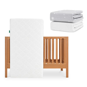 The Newton Baby Galileo Crib stands upright with the Original Crib Mattress inside. Above and to the right, two Newton Baby sheets—one gray with white stars and one plain white—are neatly stacked. skip