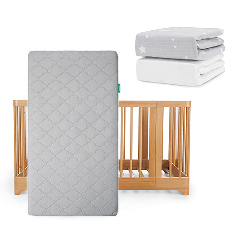 The Newton Baby Nest Convertible Crib, Original Mattress, & Sheets set includes a wooden crib with grey mattress, plus two folded fitted sheets—one plain white and one Breathable Organic Cotton Sheet with white stars.