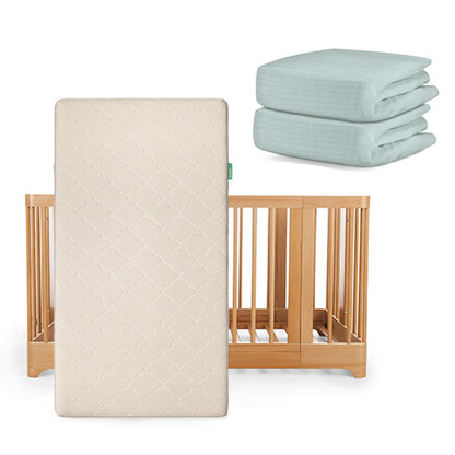 The Newton Baby Nest Convertible Crib with the Original Mattress is shown in light wood, paired with two folded light blue sheets—product set includes crib, mattress, and sheets.