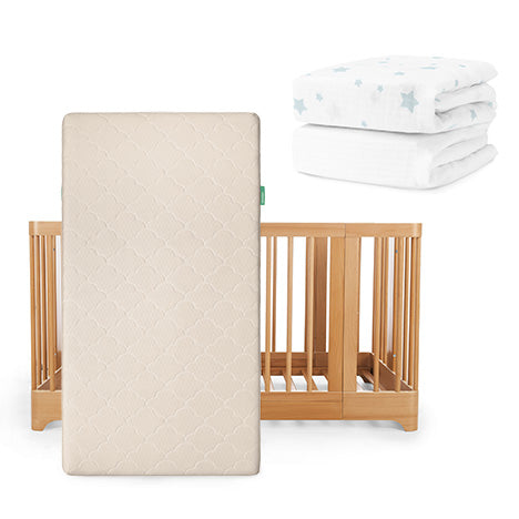 A Newton Baby Nest Convertible Crib with an Original Mattress stands upright, while two folded white Sheets with blue stars sit in the background.