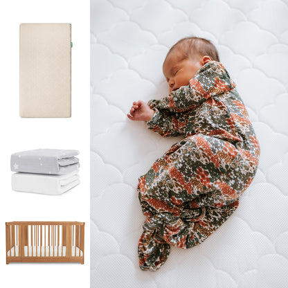 A baby in a floral-patterned sleeper lies on the Newton Baby Nest Convertible Crib with Original Mattress and Sheets, atop a white quilt. To the left are images of the crib set, folded blankets, and a breathable organic cotton sheet. 111-8420-CST-1000-SAN-SGW
