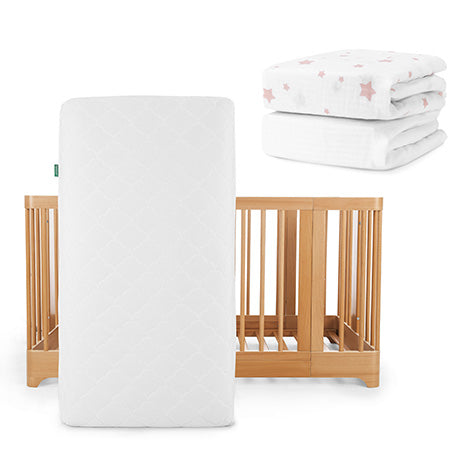 A Newton Baby Nest Convertible Crib with Original Mattress stands upright; in the top right are two folded white sheets, including one pink star-patterned Breathable Organic Cotton Sheet.