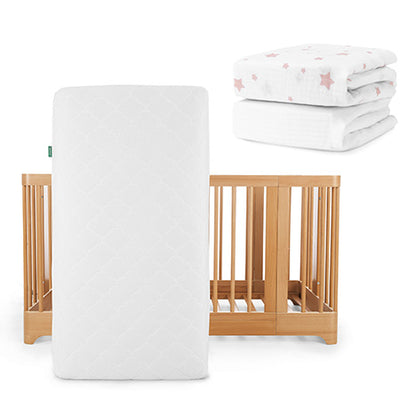A Newton Baby Nest Convertible Crib with Original Mattress stands upright; in the top right are two folded white sheets, including one pink star-patterned Breathable Organic Cotton Sheet.