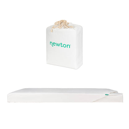 A white Newton Baby Bundle 1 BFCM crib mattress with a removable cover is shown lying flat, with its carrying/storage bag placed above it.