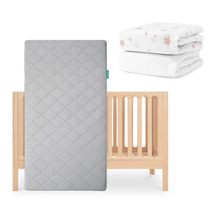 The Galileo Crib by Newton Baby, with the Original breathable crib mattress in gray, stands upright. At the top right, two folded fitted sheets—one plain white and one with pink stars—include an organic cotton sheet from Newton Baby. skip