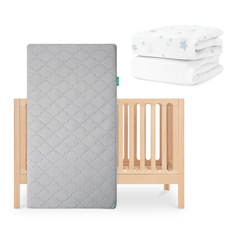 The Newton Baby Galileo Crib in light wood is shown with the Original Crib Mattress in gray, plus two folded sheets—one white and one organic cotton with blue stars—displayed on a white background. skip