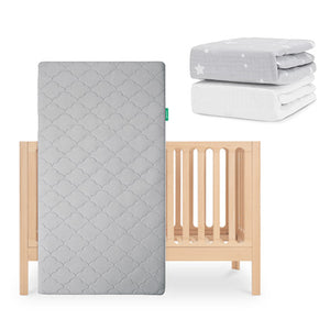 The Newton Baby Galileo Crib stands upright with the Original Crib Mattress (gray-patterned, breathable). Two folded sheets—one gray with white stars and one organic cotton—are placed above and to the right of the crib. skip