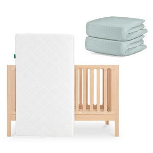 The Newton Baby Galileo Crib is shown with the Original Crib Mattress propped against it and two folded Newton Baby cotton sheets stacked neatly beside the crib. skip