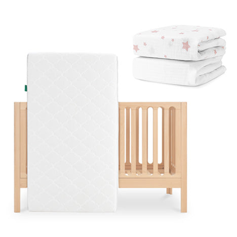 The Newton Baby Galileo Crib in light wood with the Original Crib Mattress is pictured, alongside a folded stack of organic cotton sheets featuring a pink star pattern. skip