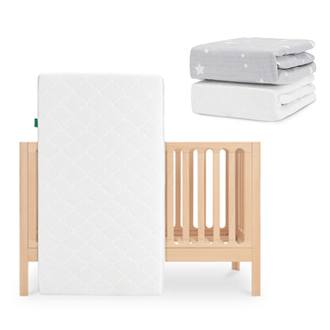 The Newton Baby Galileo Crib in light wood has the Original Crib Mattress, which is white and breathable, leaning against it. On top are two folded Newton Baby sheets: one gray with white stars and one organic cotton sheet. skip