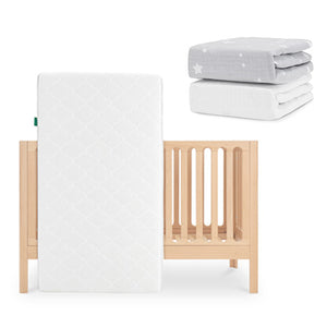 The Newton Baby Galileo Crib in light wood has the Original Crib Mattress, which is white and breathable, leaning against it. On top are two folded Newton Baby sheets: one gray with white stars and one organic cotton sheet. skip