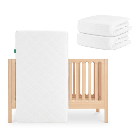 The Newton Baby Galileo Crib in light wood is paired with the Original Crib Mattress propped against it and two stacks of organic cotton sheets, all arranged on a plain white background.
skip