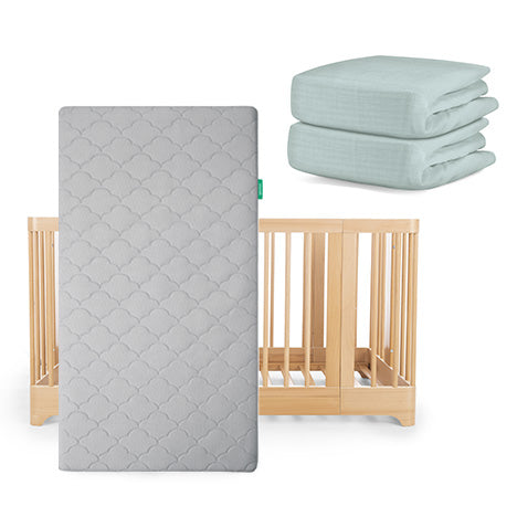 The Newton Baby Nest Convertible Crib with the Original Mattress has two light green fitted sheets from the Nest Sleep Bundle stacked nearby.