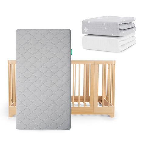 The Newton Baby Nest Convertible Crib, Original Mattress, and Sheets set includes a grey crib with mattress and two folded sheets—one grey with white stars and one plain white—stacked neatly beside it.