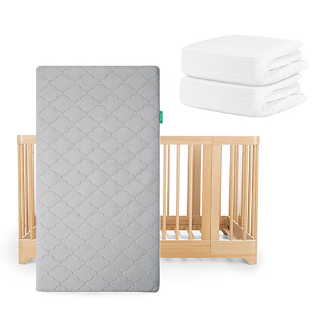 The Newton Baby Nest Convertible Crib with Original Mattress leans against a white background, with two folded Breathable Organic Cotton Sheets stacked nearby.