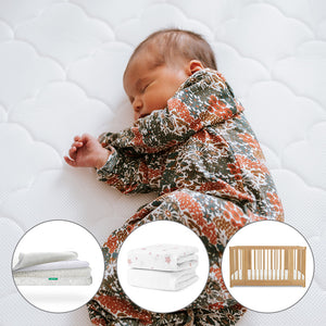 A baby sleeps on the Newton Baby Nest Convertible Crib with the Original Mattress, wearing a floral onesie. Insets below show a Breathable Organic Cotton Sheet, a star blanket, and the Nest Convertible Crib.