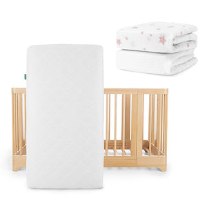 A Newton Baby Nest Convertible Crib with an Original Mattress is displayed beside two folded Breathable Organic Cotton Sheets in a pink star print.