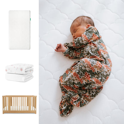 A baby in a floral onesie sleeps on the Newton Baby Nest Convertible Crib with the Original Mattress and Breathable Organic Cotton Sheet. To the left are images of the white mattress, star-patterned blankets, and crib. 111-8420-NAT-1000-WHT-PSW